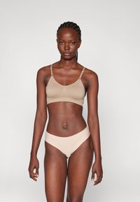 Bralette bege com alças ajustáveis e uma textura suave, combinando com cuecas de biquíni bege a condizer, com um design minimalista.