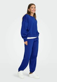 Niebieska bluza i pasujące dresy wykonane z miękkiej, fakturowanej tkaniny. Bluza ma luźny krój i prążkowane mankiety; dresy mają elastyczne nogawki.