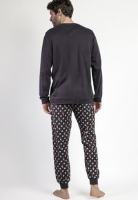Camiseta de manga larga gris oscuro con cuello redondo, combinada con pantalones de pijama negros que presentan un patrón repetido de diseños en rojo y blanco y puños elásticos.