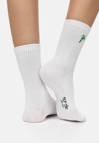 Calcetines de algodón blancos de caña corta con textura acanalada y un bordado de palmera verde en el lado. Texto en negro que indica la talla en la suela.