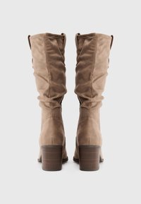 Botas altas de ante color canela con un diseño arrugado, que cuentan con punta redondeada y un tacón grueso y apilado.