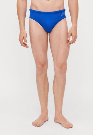 Slip da nuoto blu realizzati in tessuto liscio, caratterizzati da cuciture minime e una cintura elastica, con un piccolo logo sul lato sinistro anteriore.