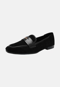 Mocassin en suede noir avec une sangle en cuir noir et un petit détail décoratif en or sur fond blanc.