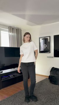 Valge lühikeste varrukatega topp, kergelt lõhikuga, kombineeritud mustade kitsaste teksapükstega ja mustade platvormsaabastega. Lihtne disain, sile tekstuur.