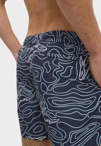 Zwemshorts met een marineblauwe basis en een witte golvende lijnpatroon. Gemaakt van lichtgewicht stof, ze hebben een elastische tailleband en een achterzak.