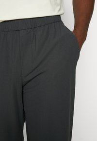Dunkelgraue Hose mit elastischem Bund, seitlichen Taschen und feiner Textur. Leichter Stoff, geeignet für die Freizeit.
