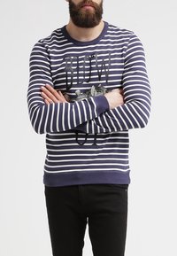 Sudadera de manga larga a rayas en azul marino y blanco con cuello redondo, texto gráfico y un diseño texturizado en la parte delantera.