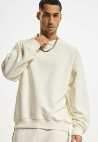 Creme sweatshirt lavet af blødt stof, med rund hals, ribbede manchetter og kant. Inkluderer en metallisk kæde halskæde som tilbehør.