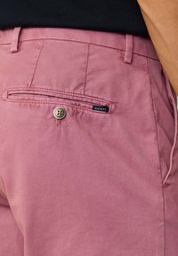 Ružičaste pamučne hlače s stražnjim džepom koji se zatvara dugmetom i oznakom marke. Glatka tekstura, krojeni fit i vidljivi šavovi.
