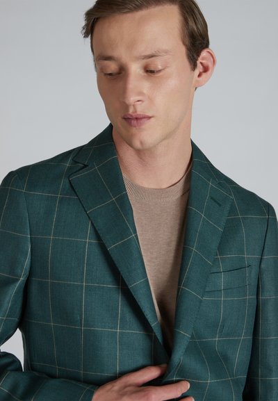 TURKUSOWA marynarka w kratkę z jasnobeżowymi liniami, wykonana z teksturowanej tkaniny, zestawiona z beżowym swetrem pod spodem.