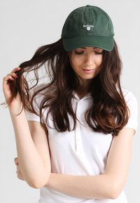 Dunkelgrüne Baseballmütze mit gesticktem "Barbour"-Logo auf der Vorderseite, strukturierte Krone und gebogenem Schirm. Einfarbiger Stoff, keine Muster.