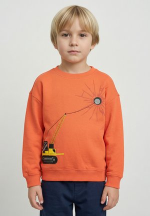 Oranssi collegepaita, jossa on grafiikka keltaisesta nosturista ja mustasta pyöreästä esineestä, teksturoitu kangas, lasketut olkapäät ja resorit hihansuissa.