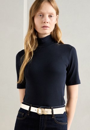 Navy ribbed turtleneck top with short sleeves, paired with high-waisted dark jeans and a light-colored belt featuring a circular buckle.