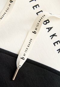 Schwarz-weißes Sweatshirt mit strukturierter Oberfläche. Mit geprägtem "TED BAKER"-Logo. Stoffetikett mit der Aufschrift "b by TED BAKER" in schwarzer Schrift.