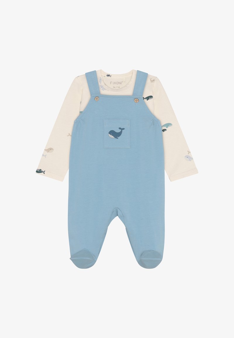 Salopette en coton bleu avec des bretelles à boutons et une poche avant ornée d'un motif de baleine. En dessous, un t-shirt à manches longues crème avec de petits motifs de poissons.