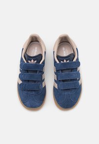 Tummansiniset nubuck-kengät kolmella tarranauhalla, beigeillä yksityiskohdilla ja kumipohjalla, jossa on logo kielekkeessä ja sisäpohjassa.