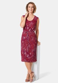 Rotes Kleid ohne Ärmel mit Blumenmuster und tailliertem Schnitt, aus strukturiertem Stoff. Kombiniert mit rosa High-Heel-Sandalen.