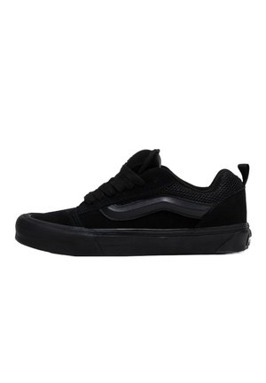 Schwarzer Low-Top-Skateschuh mit vorderer Schnürung, gepolstertem Kragen, charakteristischem Seitenstreifen und strukturierter Gummisohle sowie Zehenkappe.
