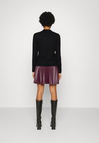 Suéter negro ajustado, falda púrpura con plisados, botas de tacón alto negras hasta la rodilla. Materiales texturizados con costuras visibles y una silueta definida.