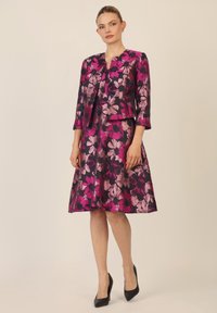 Vestido y chaqueta con estampado floral en tonos de rosa y burdeos, con falda acampanada y mangas tres cuartos. Zapatos de tacón alto negros.