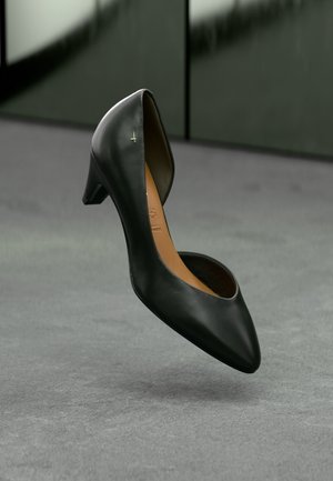 Escarpin en cuir noir avec un bout pointu, un talon bas et un léger design découpé. Il présente une semelle intérieure beige et un accent doré minimal sur le côté.