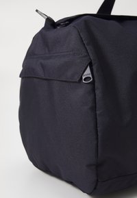 Fekete nylon táska texturált felülettel, látható elülső zsebbel és a cipzárhoz csatolt Borg logó címkével.