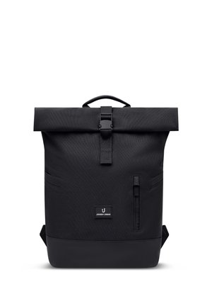 Sac à dos noir à rabat enroulé avec boucle frontale, poche zippée verticale et écusson logo "Johnny Urban" centré sur le panneau avant.