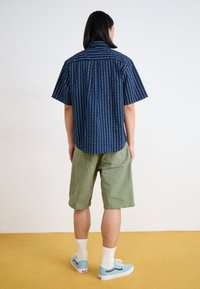 Navy short-sleeve shirt with white vertical stripes and dots, paired with olive green shorts and light blue sneakers on a yellow floor.
