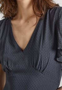 Dunkelgraues Kleid mit V-Ausschnitt, gerafften Details an der Brust und einem subtilen strukturierten Stoff mit sanften Rüschendetails an den Ärmeln.