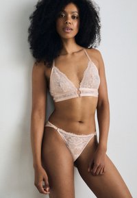 Ensemble de lingerie en dentelle rose clair comprenant un soutien-gorge triangle à bords festonnés et un string assorti avec un délicat motif floral et des bretelles ajustables.