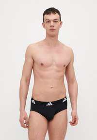 Crne gaće s bijelim Adidas logom i prugama. Izrađene od mekog materijala, s prilagodljivim krojem i elastičnom trakom za pojas.