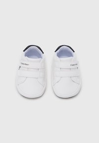 Λευκά παιδικά παπούτσια με διπλούς ιμάντες  βέλκρο· μαλακό υλικό· στρογγυλεμένη μύτη· μαύρες λεπτομέρειες στη φτέρνα· λογότυπο της μάρκας στο πλάι.