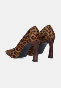 Zapatos de tacón alto con estampado de leopardo, punta afilada, pelo de animal texturizado y tacón de madera apilada. La vista lateral muestra un diseño elegante y contraste de colores.