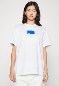 Hvid bomulds T-shirt med korte ærmer, rund halsudskæring og et blåt rektangulært logo på brystet, der står "KARL LAGERFELD JEANS."