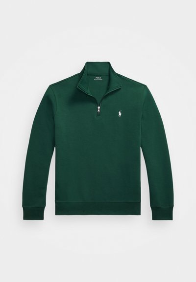 Vihreä vetoketjullinen neule, jossa on neljänneksen vetoketju, ribbikujat ja pieni brodeerattu logo rinnassa. Valmistettu pehmeästä ja sileästä kankaasta.