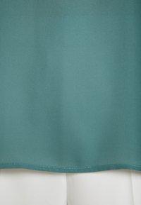 Tissu bleu sarcelle avec un ourlet cousu chevauchant un tissu blanc texturé en dessous.