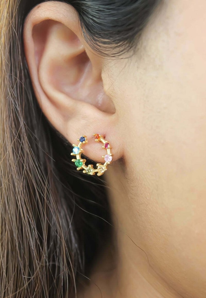 Oreille avec un anneau d'oreille en or orné de petites pierres précieuses multicolores disposées en cercle.