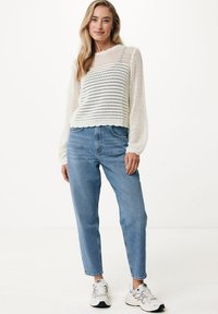 Maglione bianco lavorato a maglia con un design testurizzato e orlo a scallop, abbinato a jeans azzurri a vita alta e sneakers bianche.