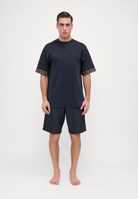 Tumši jūras zila īsām piedurknēm T-krekls ar zelta ģeometrisku rakstu uz piedurknēm, kopā ar atbilstošām tumsas šortiem, abi izgatavoti no viegla auduma.