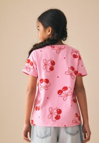 Camiseta rosa de manga corta con un estampado repetido de cerezas con acentos rojos, hecha de un tejido suave con un corte holgado.