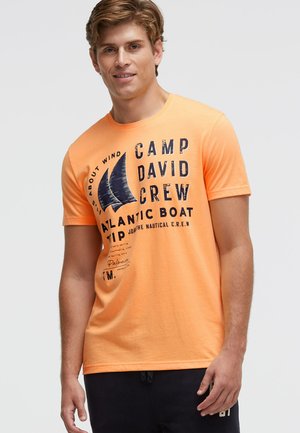 Orange cotton t-shirt with short sleeves, featuring dark blue text and sailboat graphic. Round neckline and relaxed fit design.