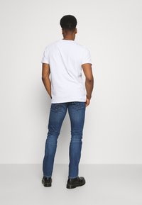 Vit t-shirt med kort ärm i kombination med åtsittande blå denimjeans. Jeansen har två bakfickor med sömdetaljer. Svarta anklarboots fulländar looken.