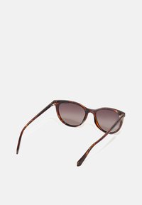 Ochelari de soare tortoise maro cu lentile degradate, rame rotunde și brațe subțiri. Prezintă un logo subtil pe tempă.