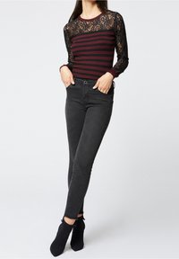 Zwarte skinny jeans gecombineerd met een bordeaux gestreept langemouwen shirt met een zwarte kanten overlay en aansluitende manchetten.