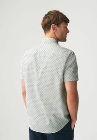 Camisa de manga corta en tela gris claro con un patrón de diamantes y cuello abotonado, con un dobladillo curvado y ventilaciones en la parte posterior.