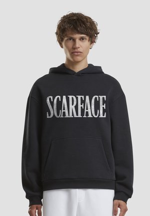 Čierna mikina s kapucňou s veľkým strieborným nápisom „SCARFACE“, obsahujúca predné vrecko a rebrované manžety. Jemná textúra látky.