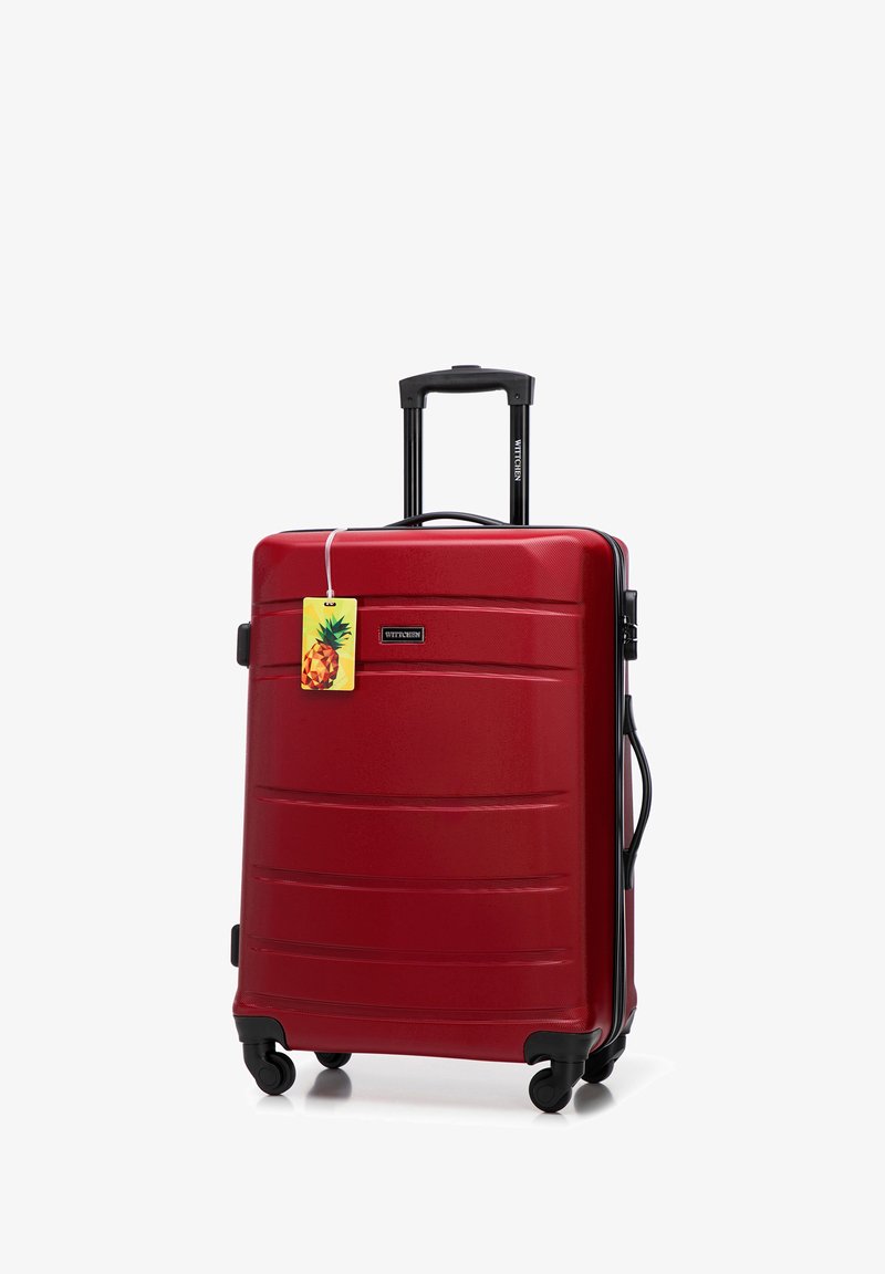 Rode harde koffer met uitschuifbare handgreep, vier draaiwielen, zijhandgreep en een bagagelabel met een ananas ontwerp eraan bevestigd.