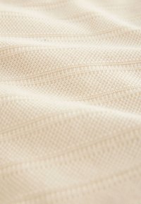 Textil mit strukturierter Oberfläche in hellem Beige, das dezente Muster und Linien zeigt und eine glatte, gewebte Stoffqualität aufweist.