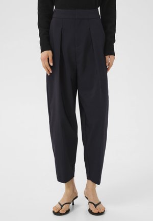 Pantaloni a pieghe navy realizzati in tessuto liscio, con vita alta, vestibilità ampia e gambe affusolate. Abbinati a infradito nere.