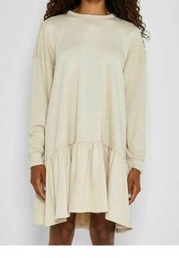Béžové dlouhé šaty s dlouhým rukávem a kulatým výstřihem, které mají rozšířený lem a zřasené detaily v pase. Měkká látka s hladkou texturou.